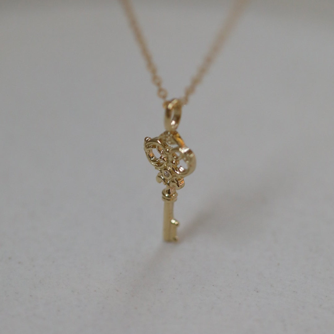 Gold key-shaped pendant on a chain against a light background