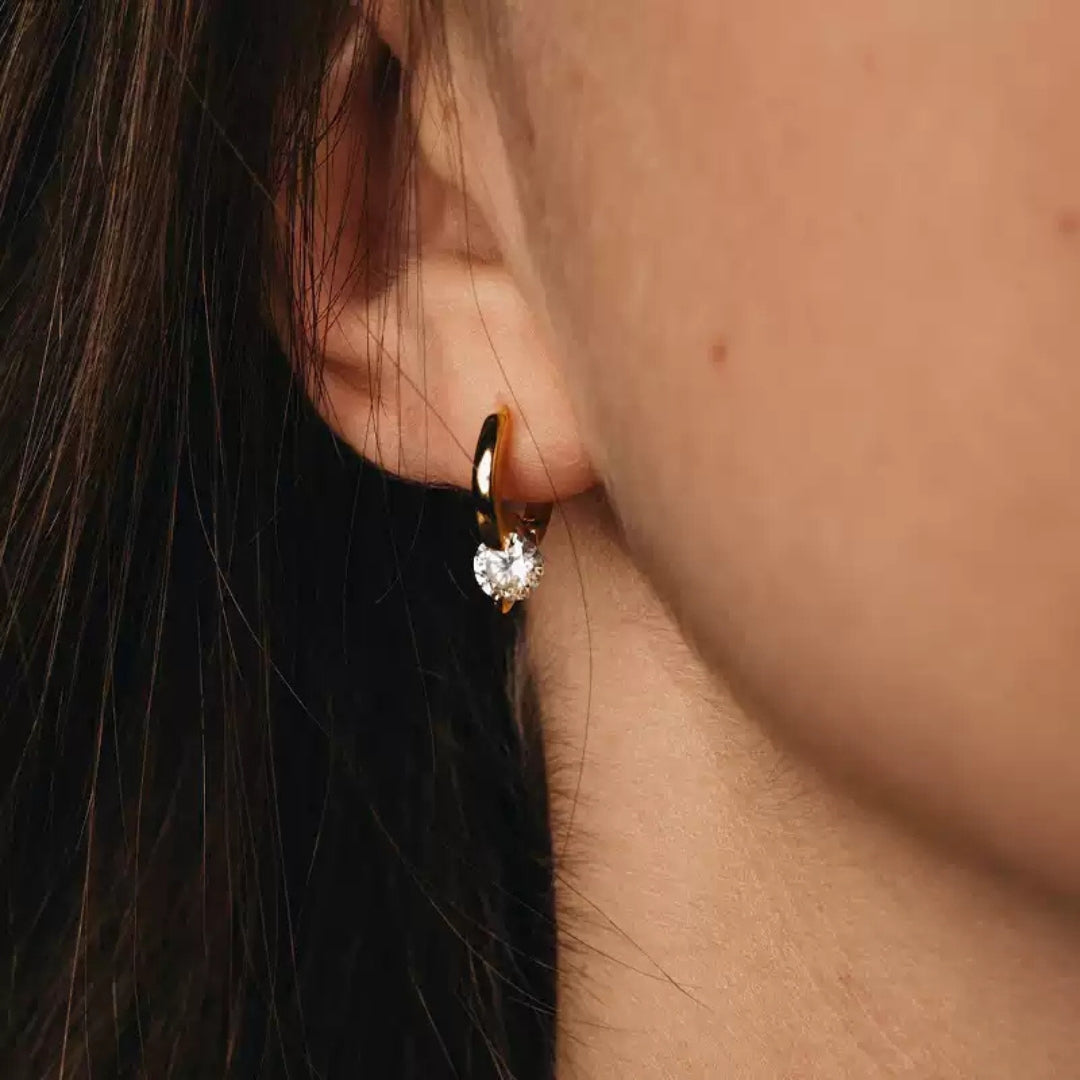 Close-up of a person wearing a gold hoop earring with a diamond.