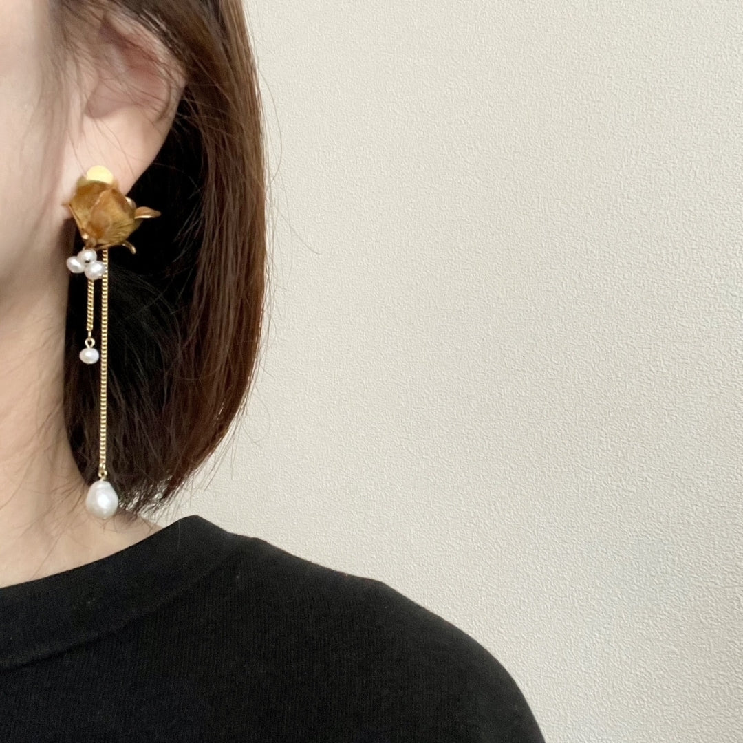 Close-up of a person wearing a gold earring with pearls against a neutral background