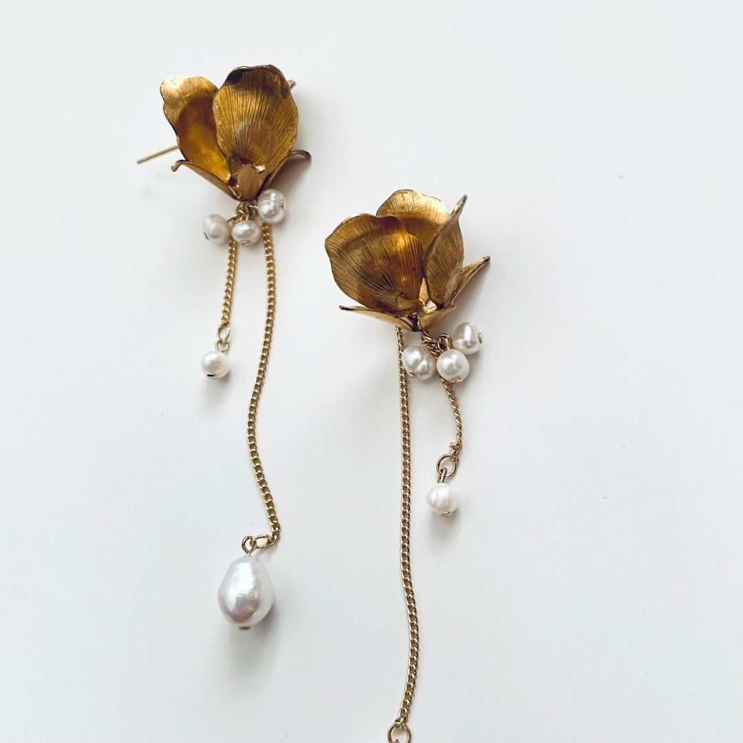 Gold flower-shaped earrings with pearl accents on a white background