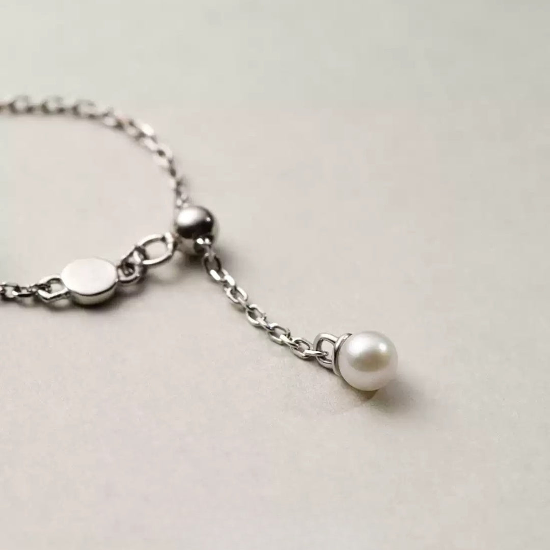 Silver chain ring with a pearl charm on a light gray background