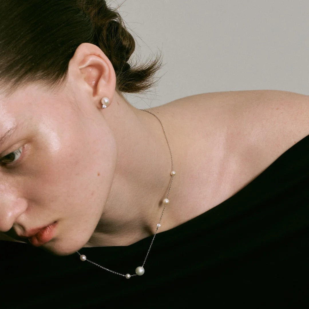 Close-up of a person wearing a delicate pearl necklace and earrings.
