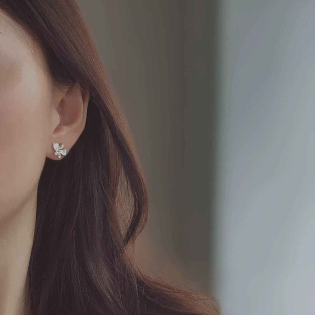 Close-up of a person wearing a delicate white flower earring with a blurred background
