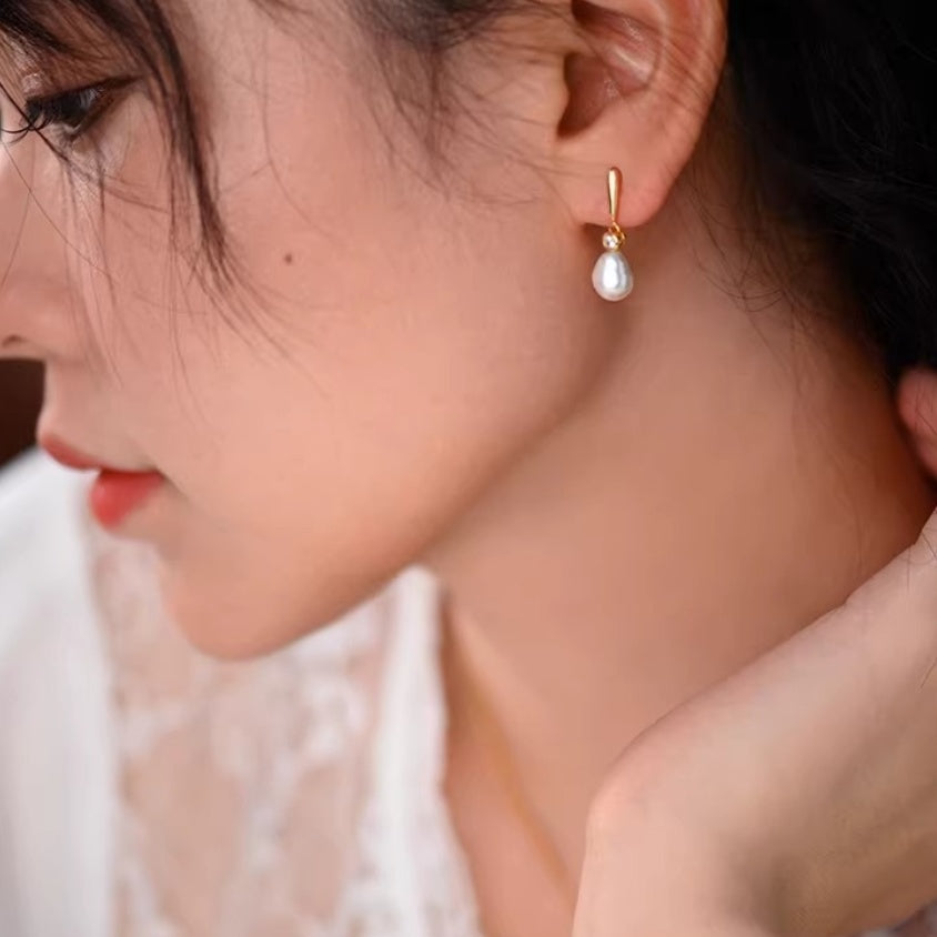 Bride wearing pearl drop earrings and a white lace dress with hands clasped, capturing a romantic wedding moment.2