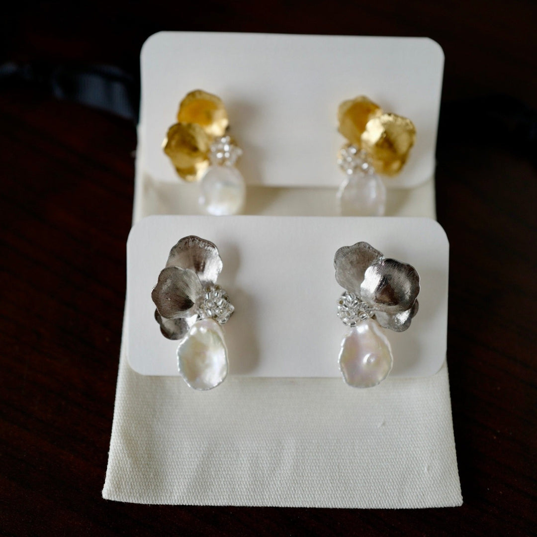 Pair of silver and gold earrings with pearls on a display card against a dark background