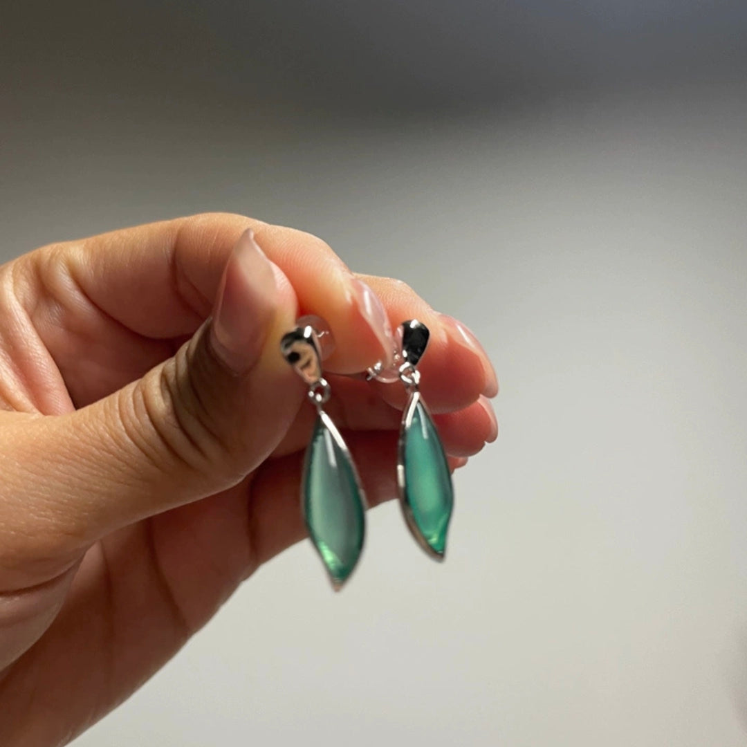 Hand holding a pair of green chrysoprase earrings against a neutral background
