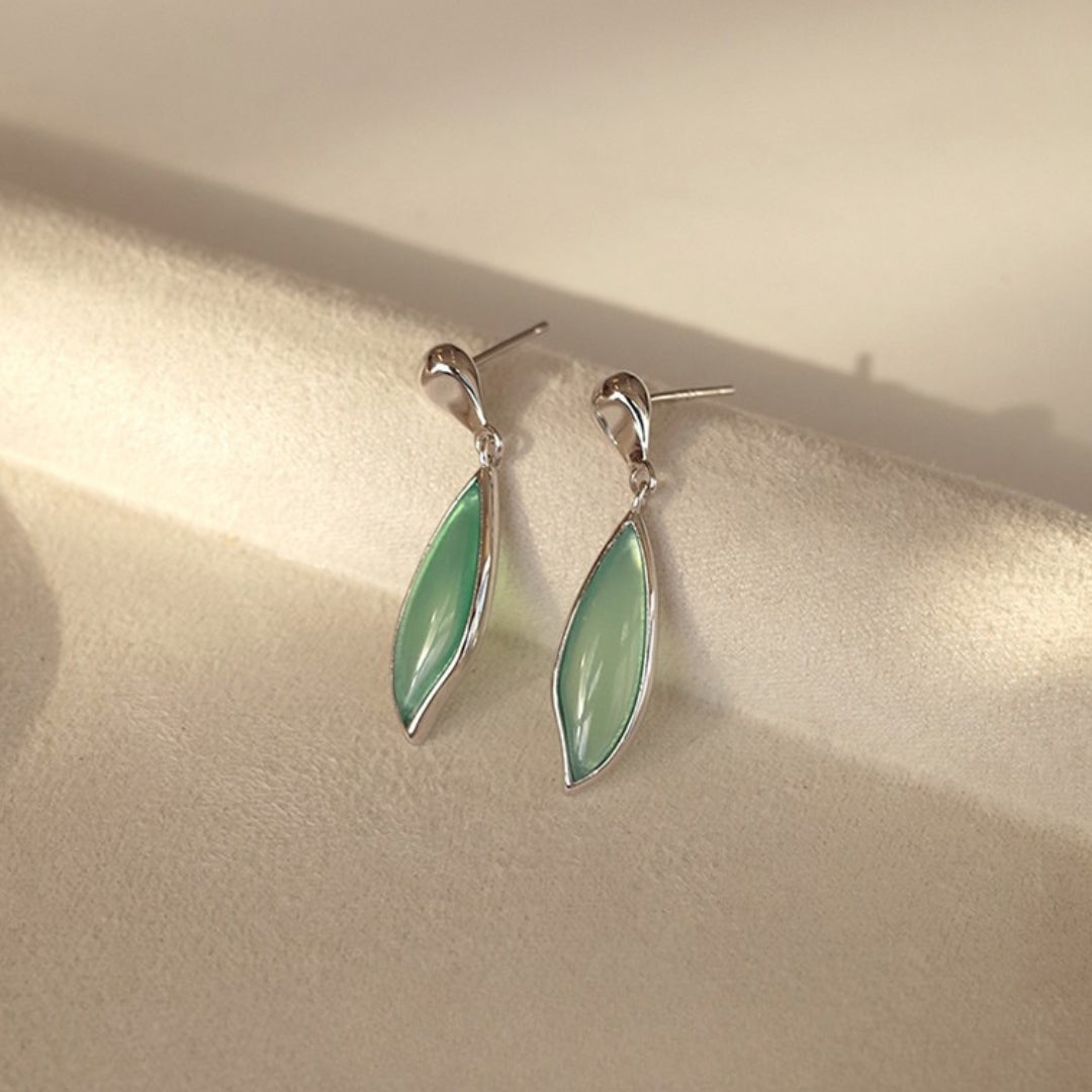 Green leaf earrings on a beige surface