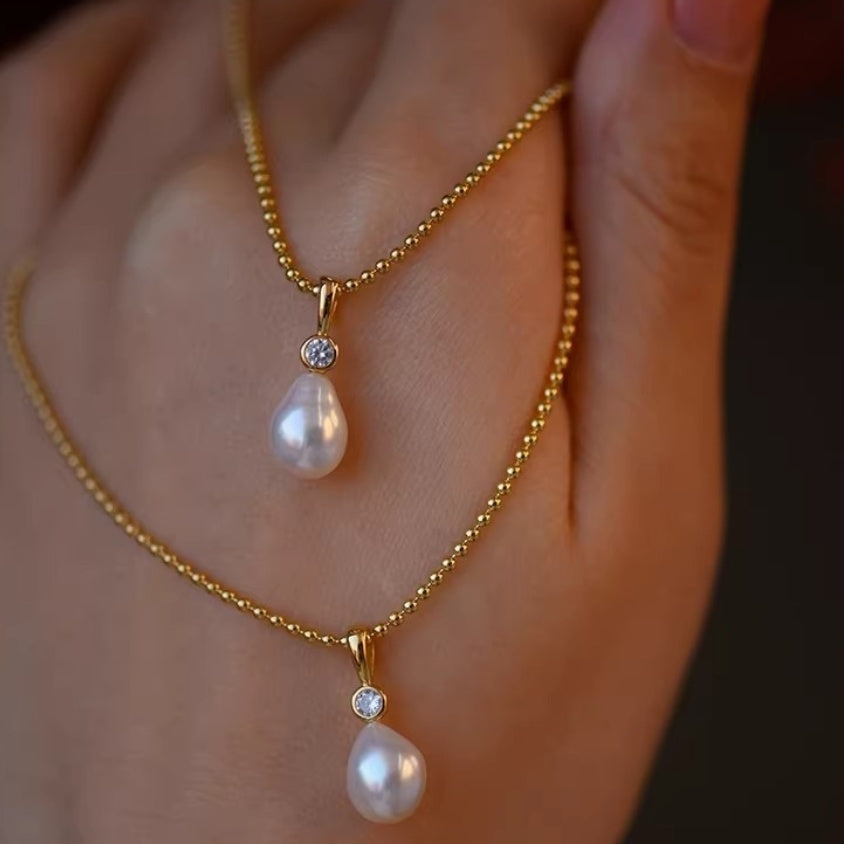 Detail shot of lustrous white teardrop pearl pendants hanging from delicate gold ball chains, showing the organic baroque shape. 3