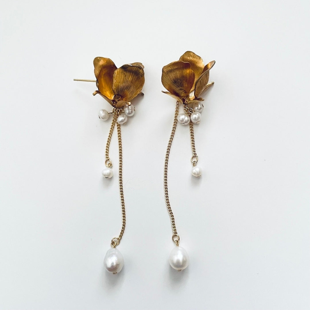 Gold floral earrings with pearl drops on a white background