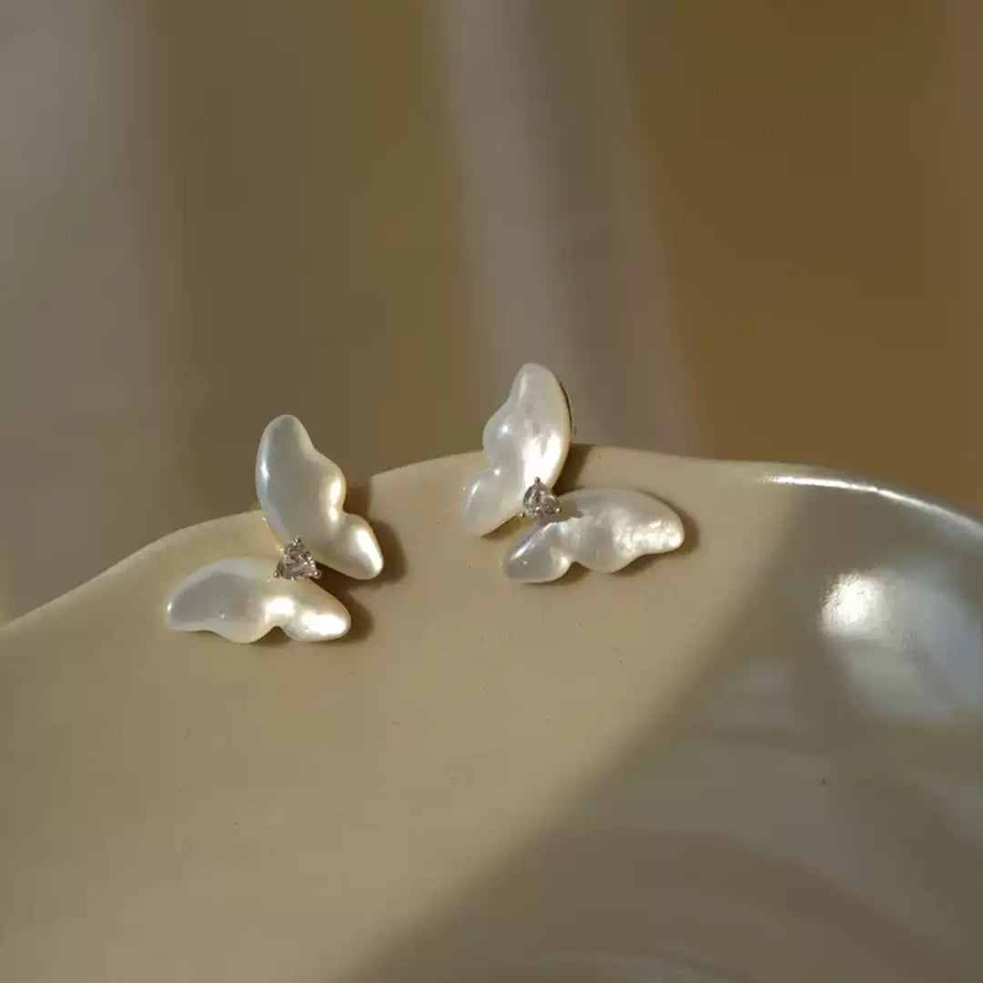 Pearl butterfly earrings on a beige surface with a soft background