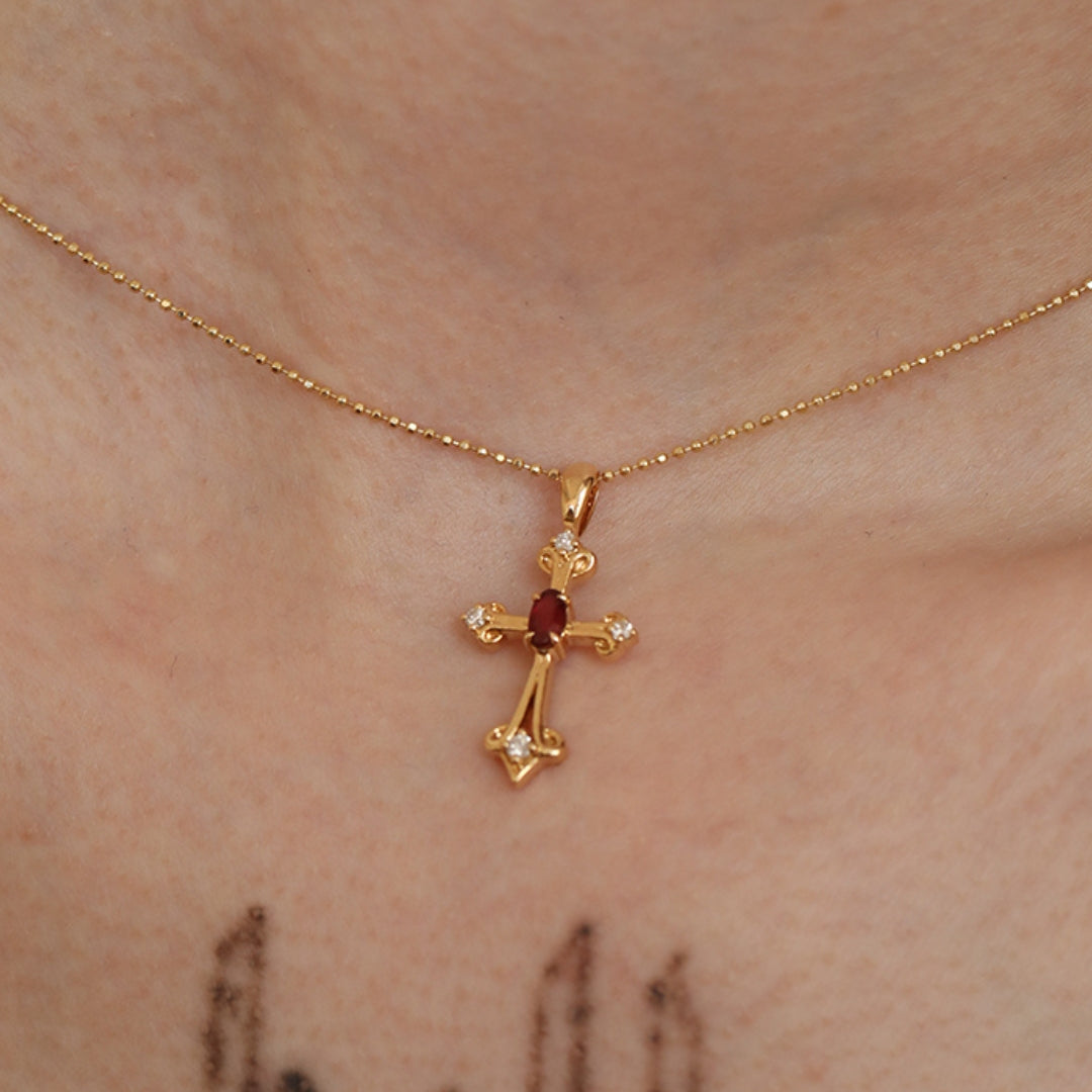 Gold cross necklace with a mozambique ruby gemstone on a person's neck