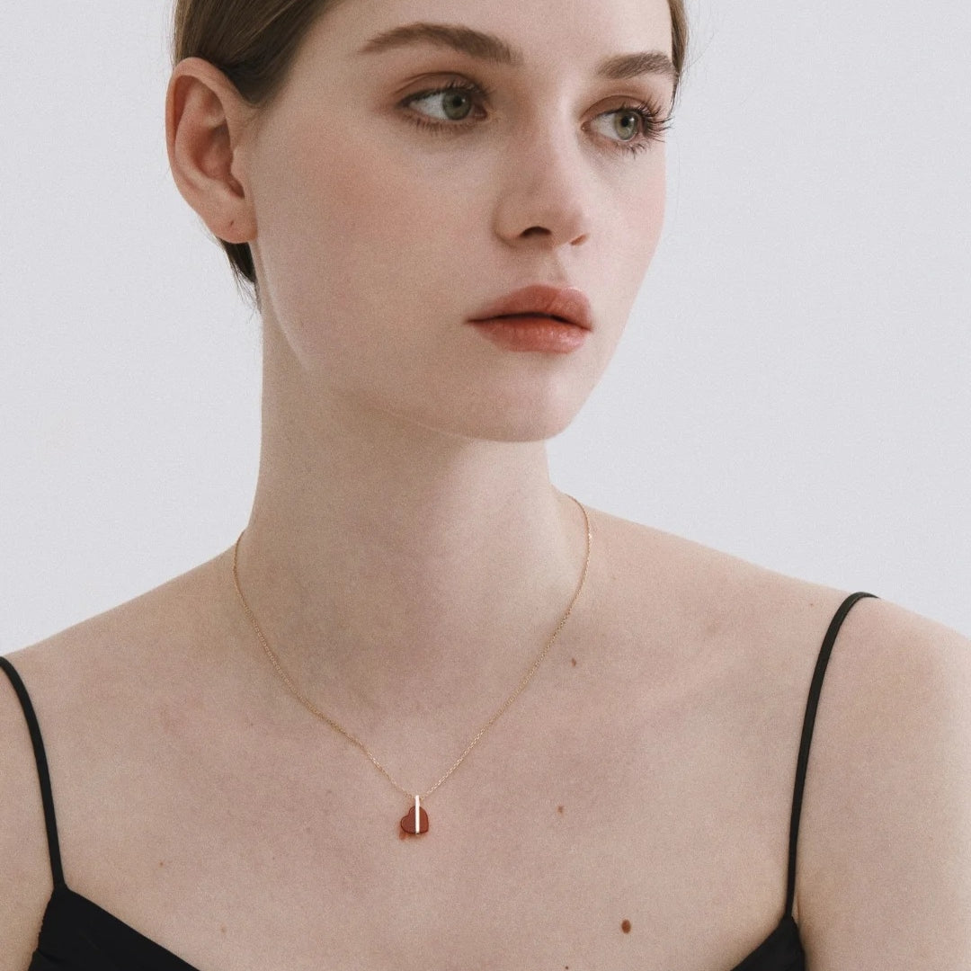 Woman wearing a gold necklace with a red heart pendant on a plain background