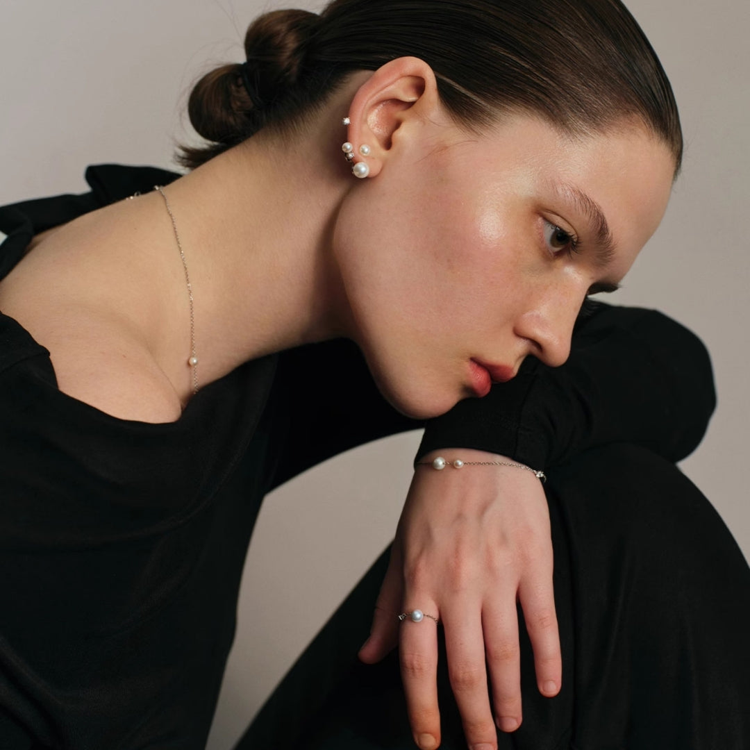 Woman wearing pearl jewelry set including earrings, a necklace, and a ring on a neutral background