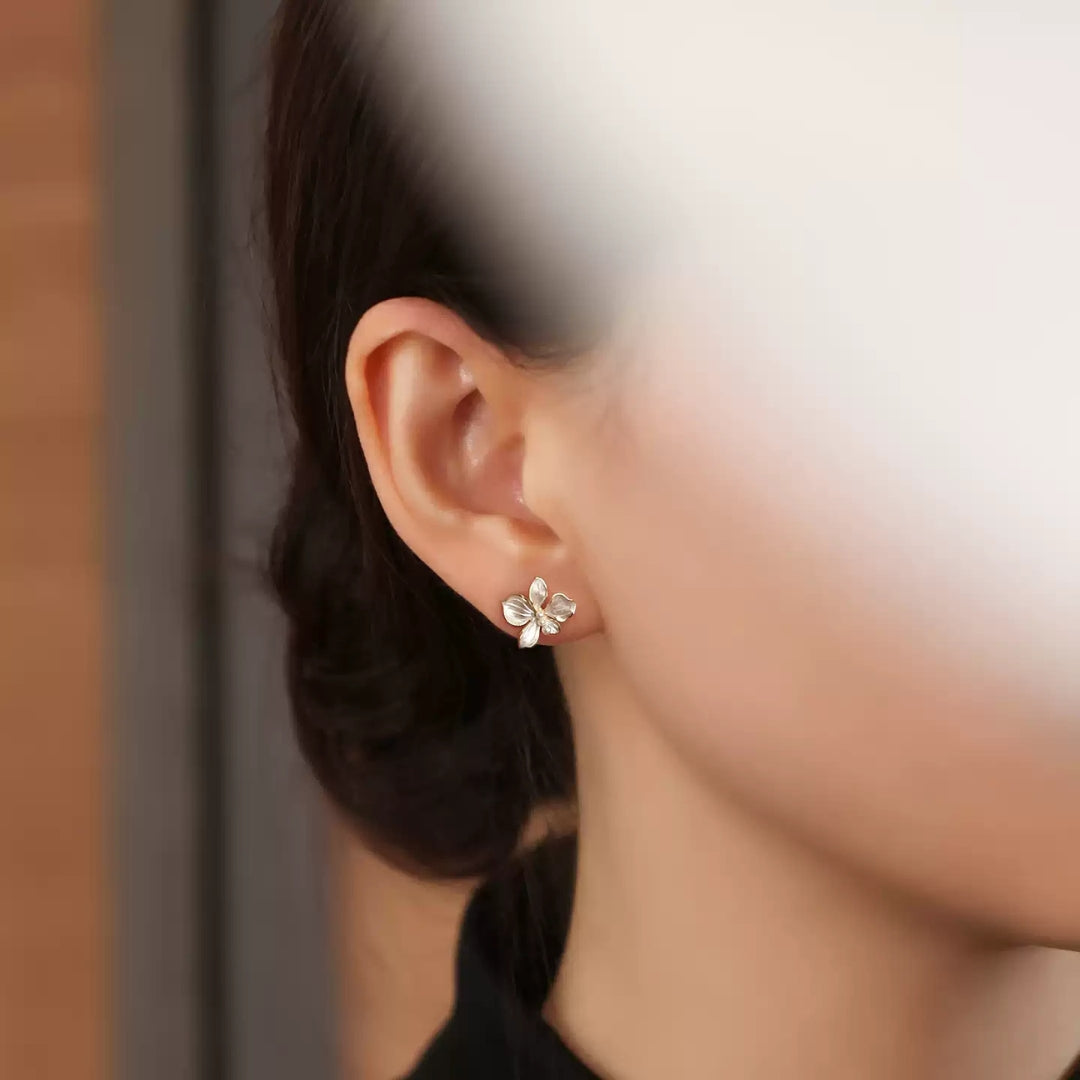 Close-up of an ear wearing a white floral earring with a blurred background