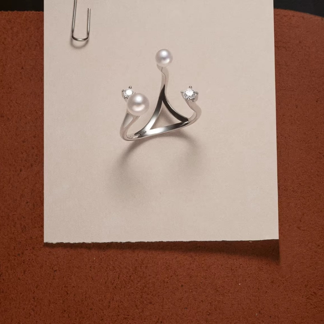 Top view of a geometric S925 sterling silver ring with two pearls and two zirconia stones on a neutral paper background, highlighting its modern architectural design.