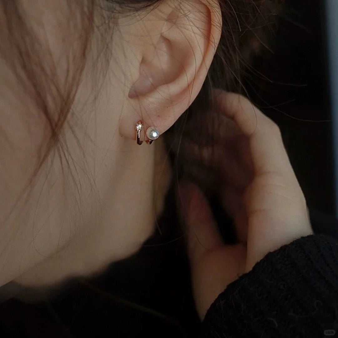 Close-up of an ear with a dainty pearl  diamond huggie earring.