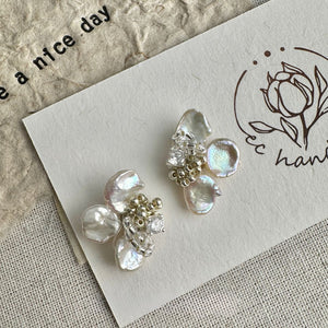 A pair of handmade statement wedding flower earrings with delicate floral designs, adorned with white pearl accents and a central baroque pearl drop, showcasing the beauty of freshwater pearl jewelry. These luxury handmade statement pearl earrings are ideal as bridal earrings pearl or elegant modern pearl earrings for any occasion.