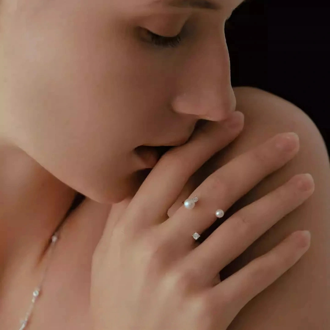 Frontal view of a woman wearing twin pearl wrap-around earrings that hug the earlobe, showing the lustrous natural pearls against a soft skin tone.