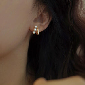 Close-up of gold bar pearl earrings featuring Tiny pearl studs arranged in a trio on Gold bar earring studs, perfect as Minimalist Wedding Earrings and Dainty elegant earrings for everyday wear.