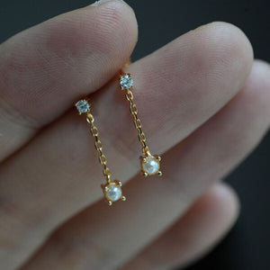 Close-up of tiny pearl and diamond short chain earrings in gold, featuring natural freshwater pearls and diamonds; elegant bridal jewelery or daily wear.