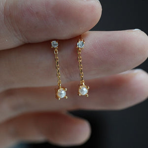 Close-up of tiny pearl and diamond short chain earrings in gold, featuring natural freshwater pearls and diamonds; elegant bridal jewelery or daily wear.