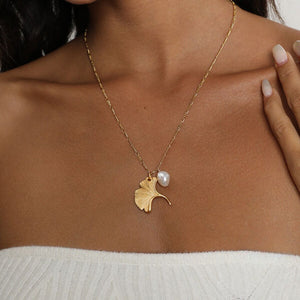 Gold ginkgo leaf necklace with a small pearl, inspired by nature and designed as an elegant botanical jewelry piece.