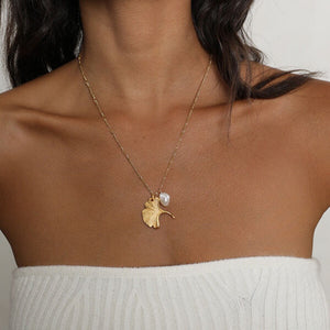 Gold ginkgo leaf necklace with a small pearl, inspired by nature and designed as an elegant botanical jewelry piece.