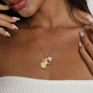 Gold ginkgo leaf necklace with a small pearl, inspired by nature and designed as an elegant botanical jewelry piece.