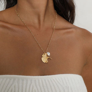 Gold ginkgo leaf necklace with a small pearl, inspired by nature and designed as an elegant botanical jewelry piece.