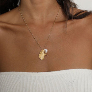 Gold ginkgo leaf necklace with a small pearl, inspired by nature and designed as an elegant botanical jewelry piece.