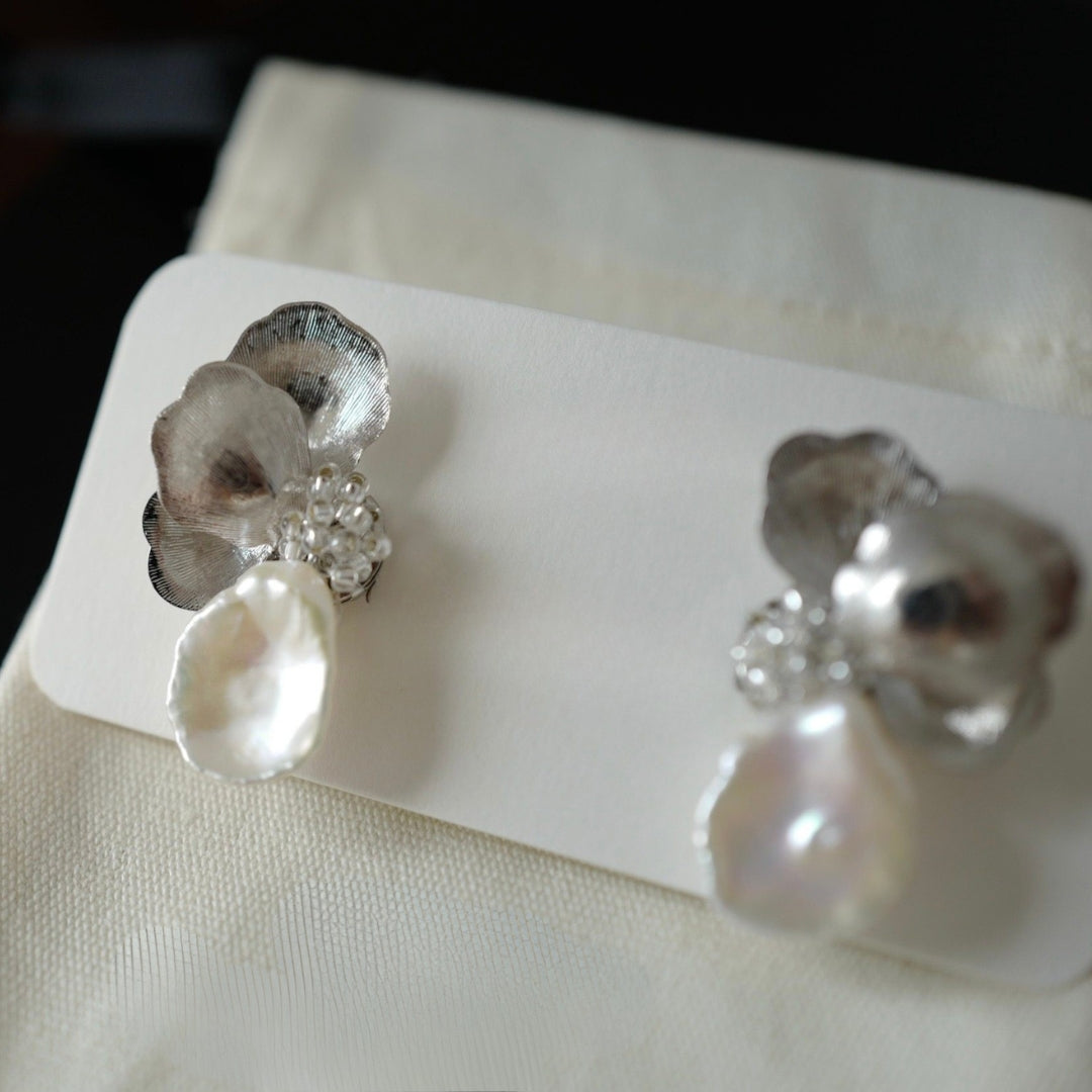 Pair of silver floral earrings with pearls on a white card.