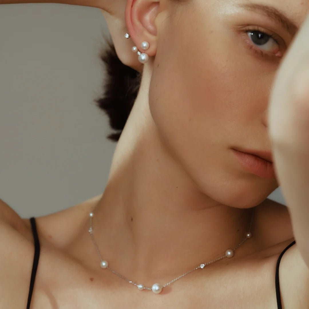 Close-up of a person wearing a pearl and diamond necklace and same set of bridal earrings against a neutral background
