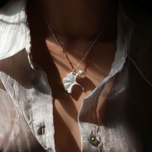 Gold ginkgo leaf necklace with a small pearl, inspired by nature and designed as an elegant botanical jewelry piece.