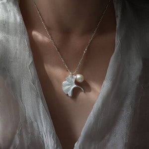 Gold ginkgo leaf necklace with a small pearl, inspired by nature and designed as an elegant botanical jewelry piece.