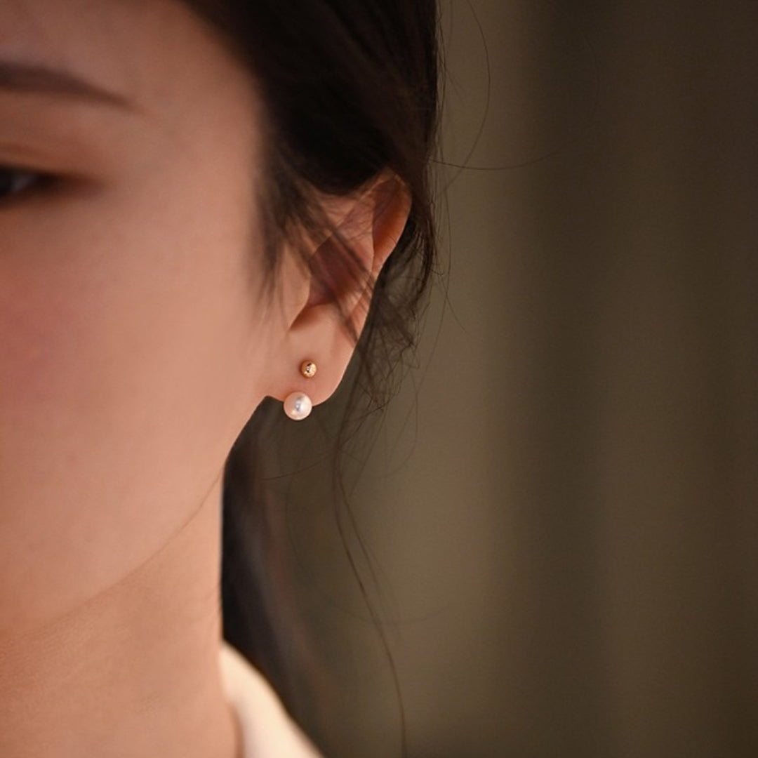 Close-up of an ear wearing a stud pearl gold earring against a blurred background