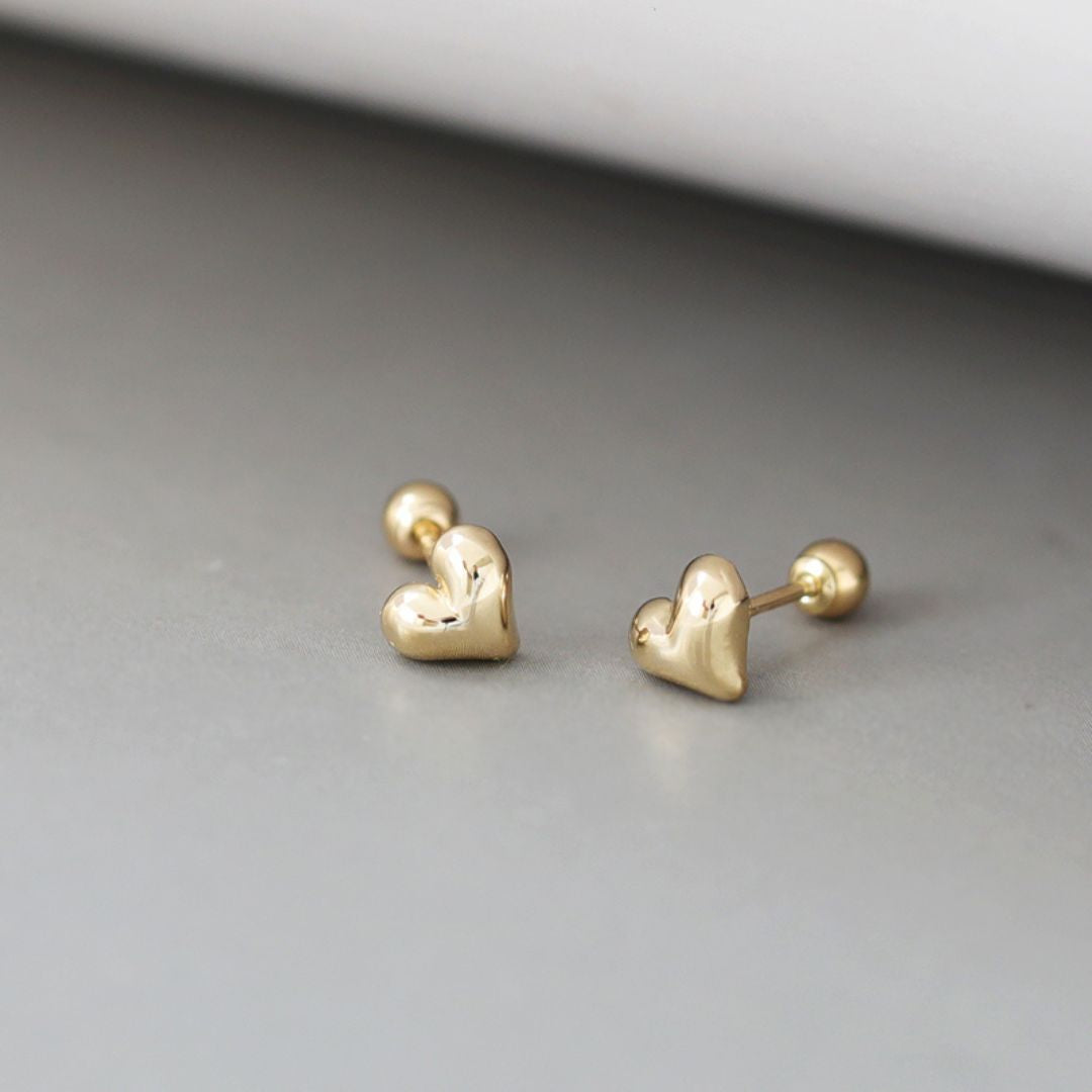 A pair of tiny gold heart studs with a delicate, minimalist design. These gold heart stud earrings showcase a classic Korean jewelry style, perfect for everyday wear.