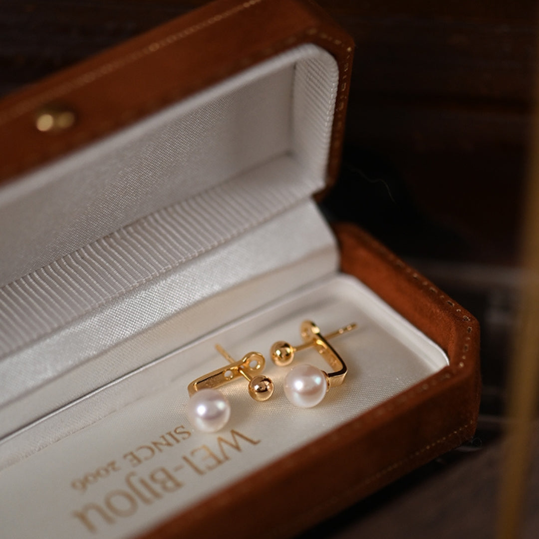 Gold pearl earrings in a leather jewelry box.