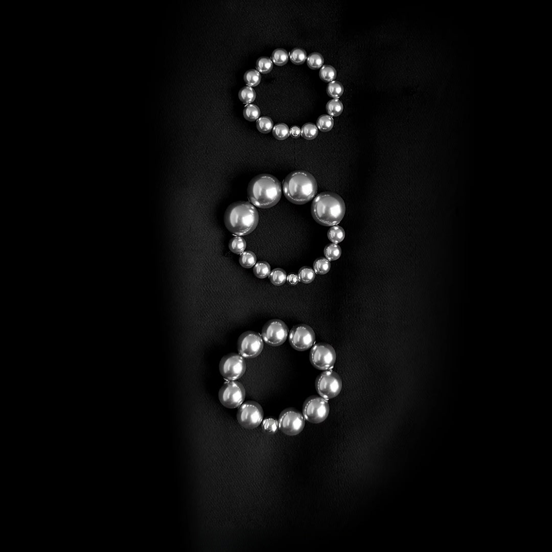 Three different sizes of white Swarovski pearl stretchy rings on black background.