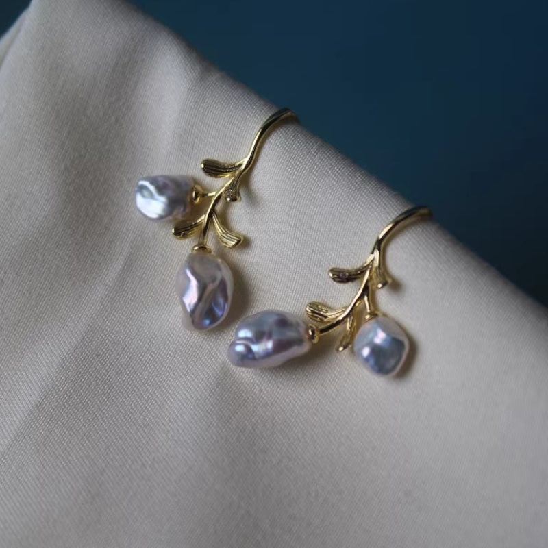 Artistic jewelry photography of handmade pearl branch earrings on a textured neutral background.